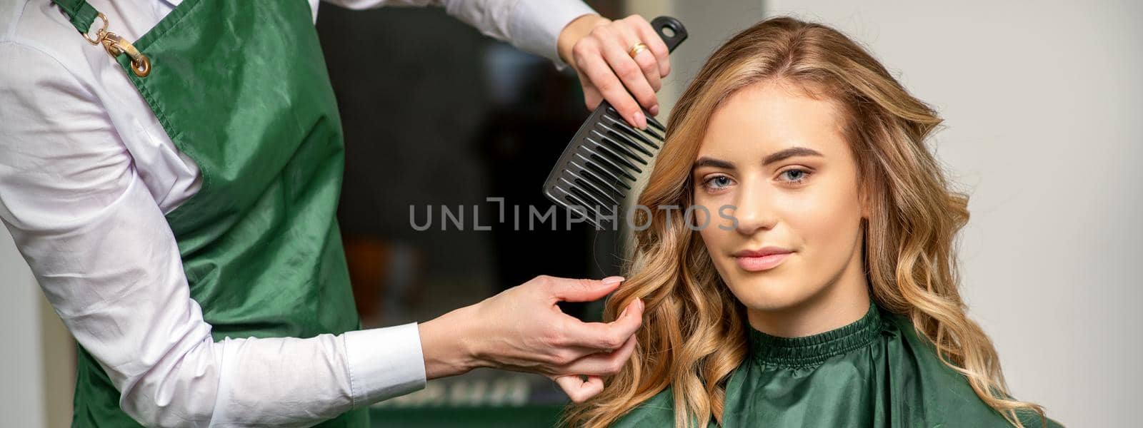 Hairdresser making hairstyling for the woman while combing with hairbrush, comb in a hair salon