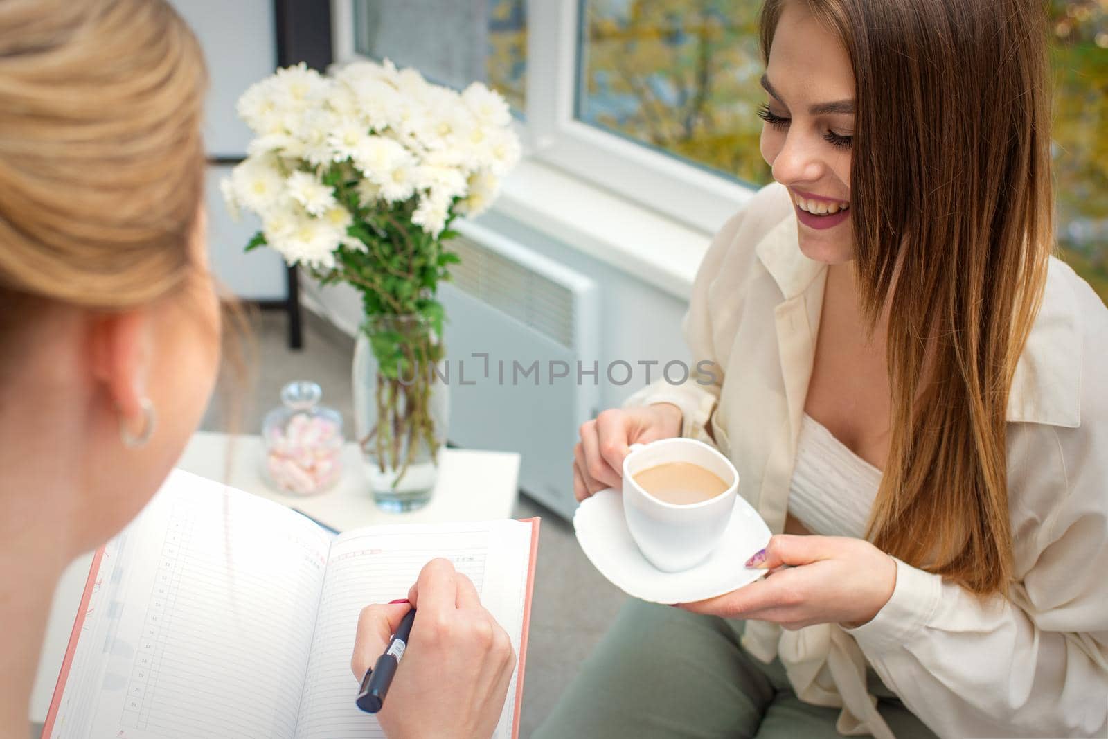 The young caucasian woman has a coffee and appointment with a female doctor in hospital office