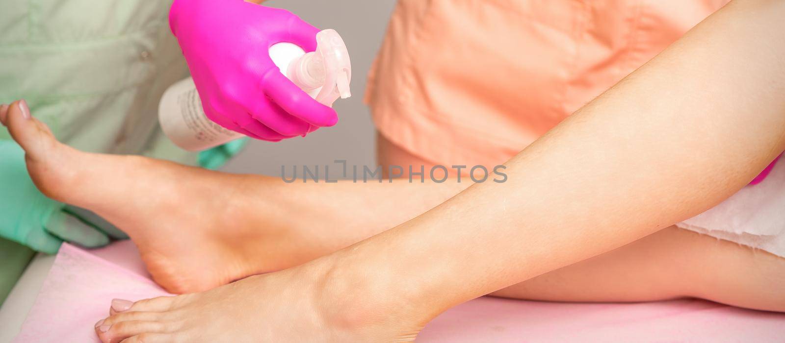 A beautician sprays a disinfectant on the feet of a young woman before the epilation procedure. Foot depilation