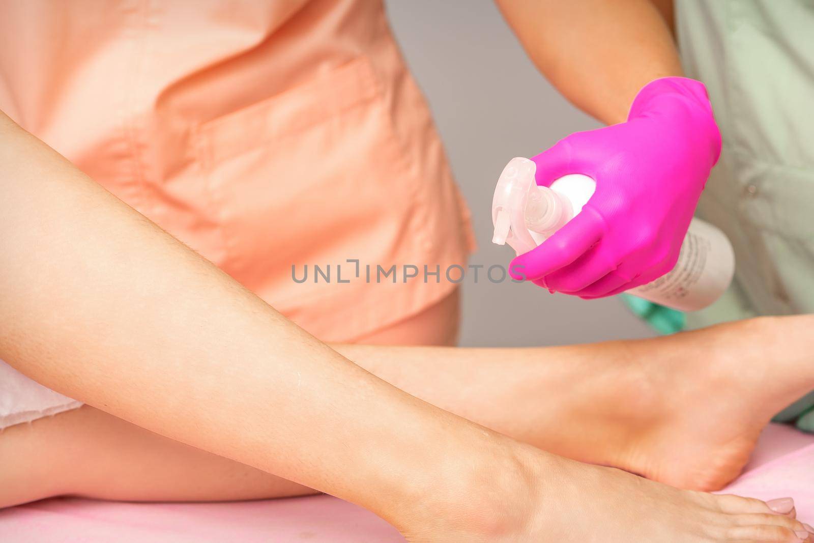 A beautician sprays a disinfectant on the feet of a young woman before the epilation procedure. Foot depilation. by okskukuruza