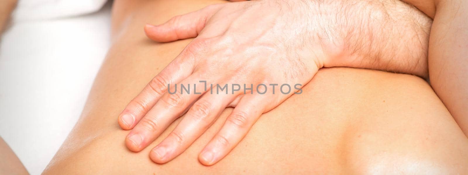 A male physiotherapist stretches the arms on the back of a man lying down, close up