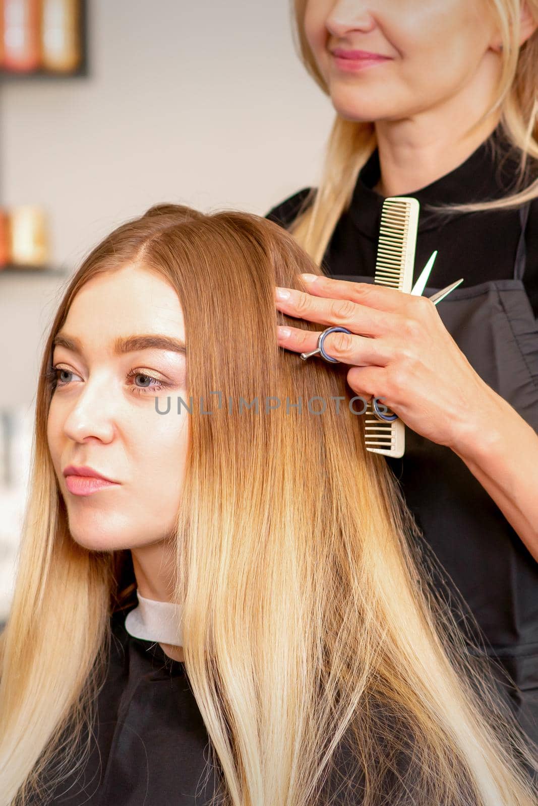 Gorgeous blonde long hair woman and her hairdresser looking and checking out hairstyle. Beautiful hairstyle of a young blonde woman after dying hair in a beauty salon, results of hair treatment
