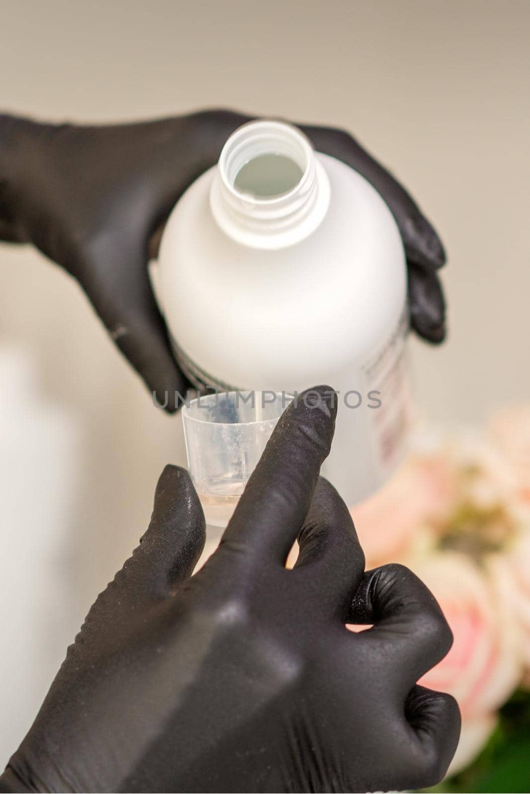 A hairdresser in black gloves is preparing hair dye with a bottle in a hair salon, close up. by okskukuruza