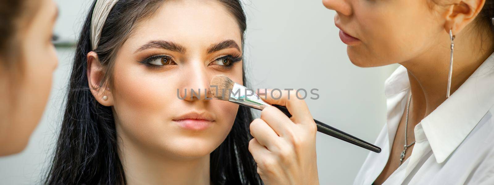 Closeup portrait of a woman applying dry cosmetic tonal foundation on the face using a makeup brush. Makeup detail