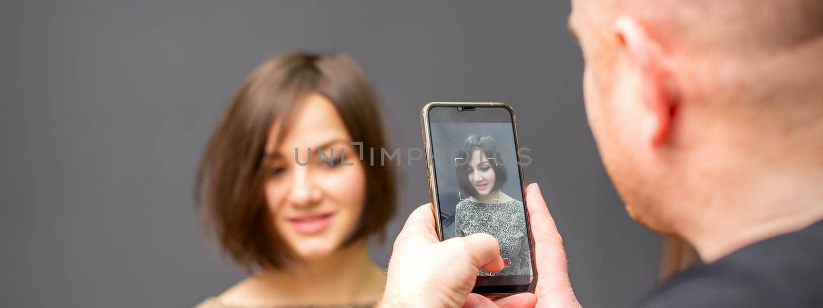 The hairdresser takes pictures of a woman finished short hairstyle on dark background