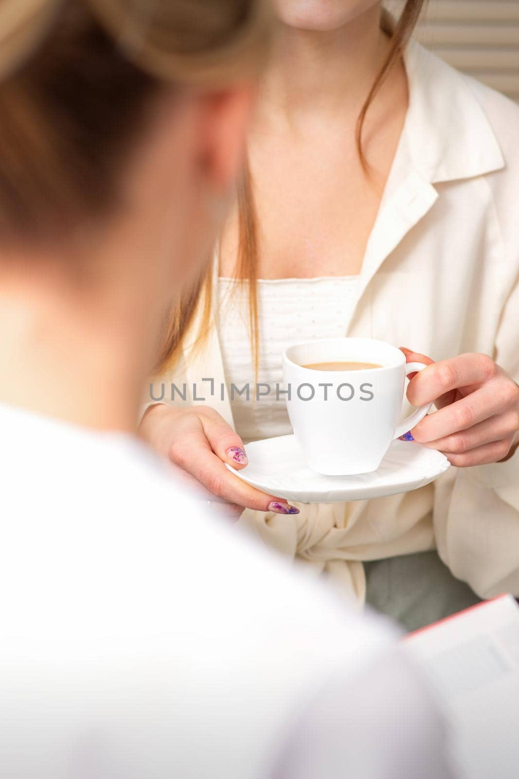 The young caucasian woman has a coffee and appointment with a female doctor in hospital office