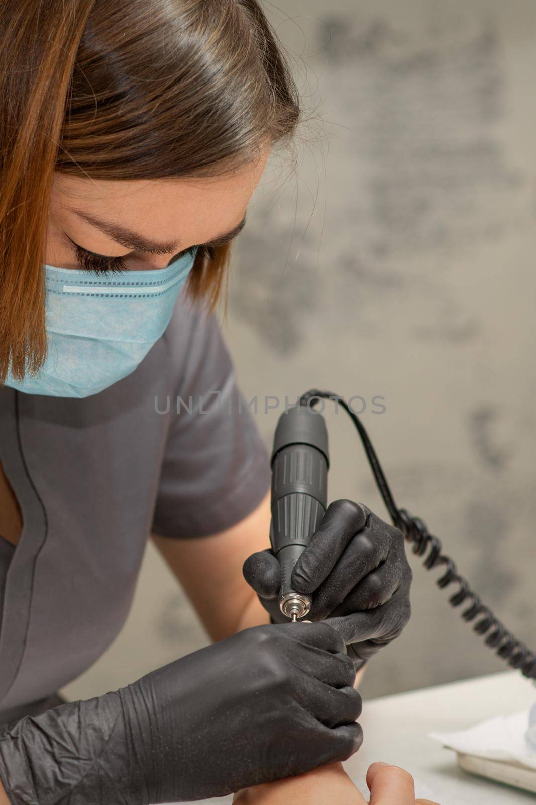 Manicurist removes nail polish uses the electric machine of the nail file during manicure in a nail salon