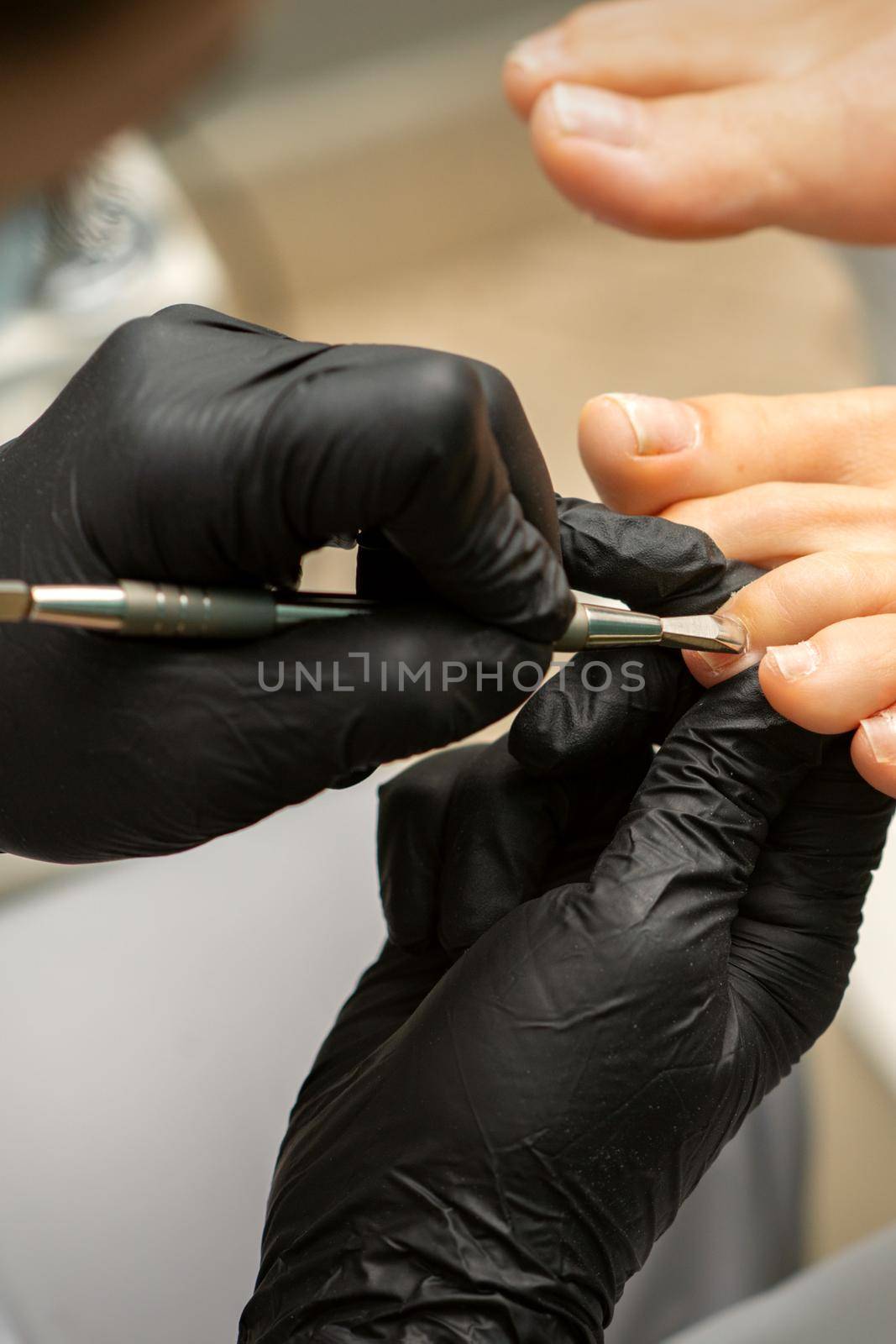 Cuticle Removal on Toes. Hands in black gloves of pedicure master remove cuticle on female toes by pusher