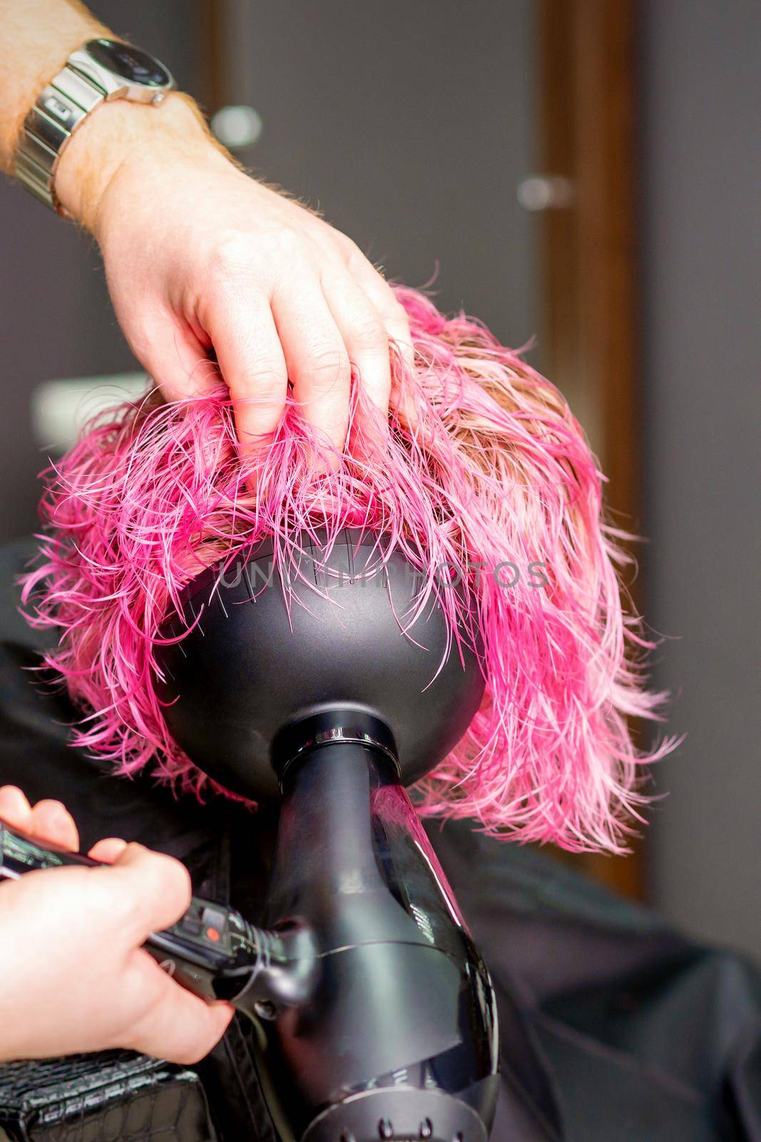 Hair Stylist making hairstyle using hair dryer blowing on wet custom pink hair at a beauty salon