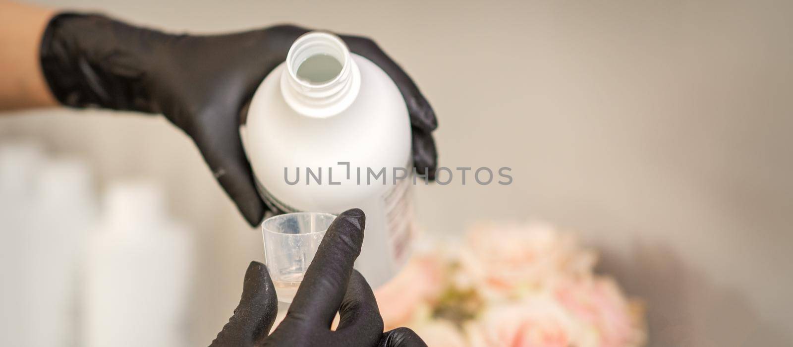 A hairdresser in black gloves is preparing hair dye with a bottle in a hair salon, close up. by okskukuruza