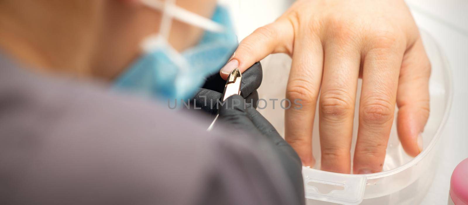Nail master removing nails cuticle with a nipper, manicure hygiene in a beauty salon