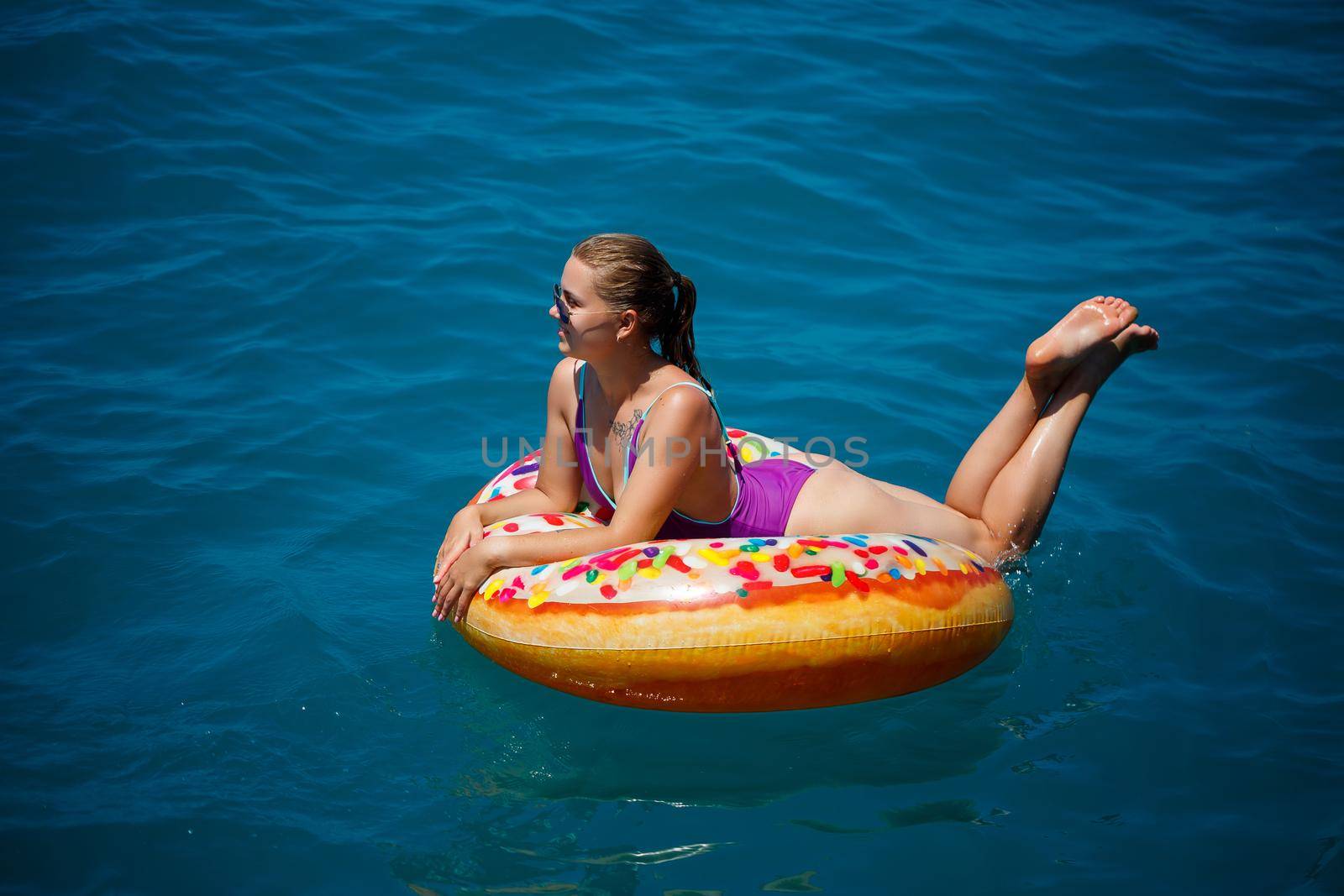 Beautiful happy young woman in a swimsuit with an inflatable ring relaxing in the blue sea. Sunny day, seaside vacation, tourism