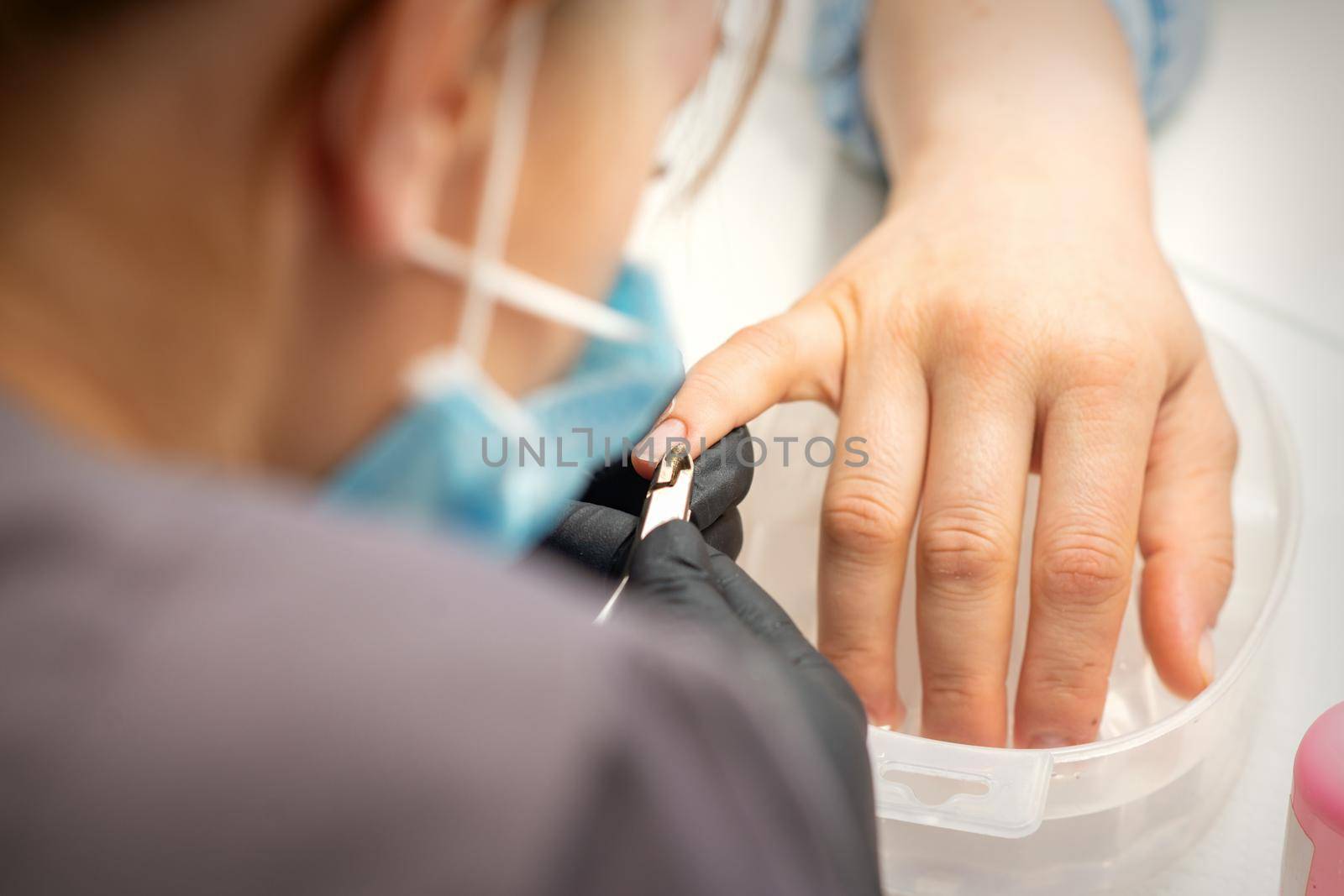 Nail master removing nails cuticle with a nipper, manicure hygiene in a beauty salon
