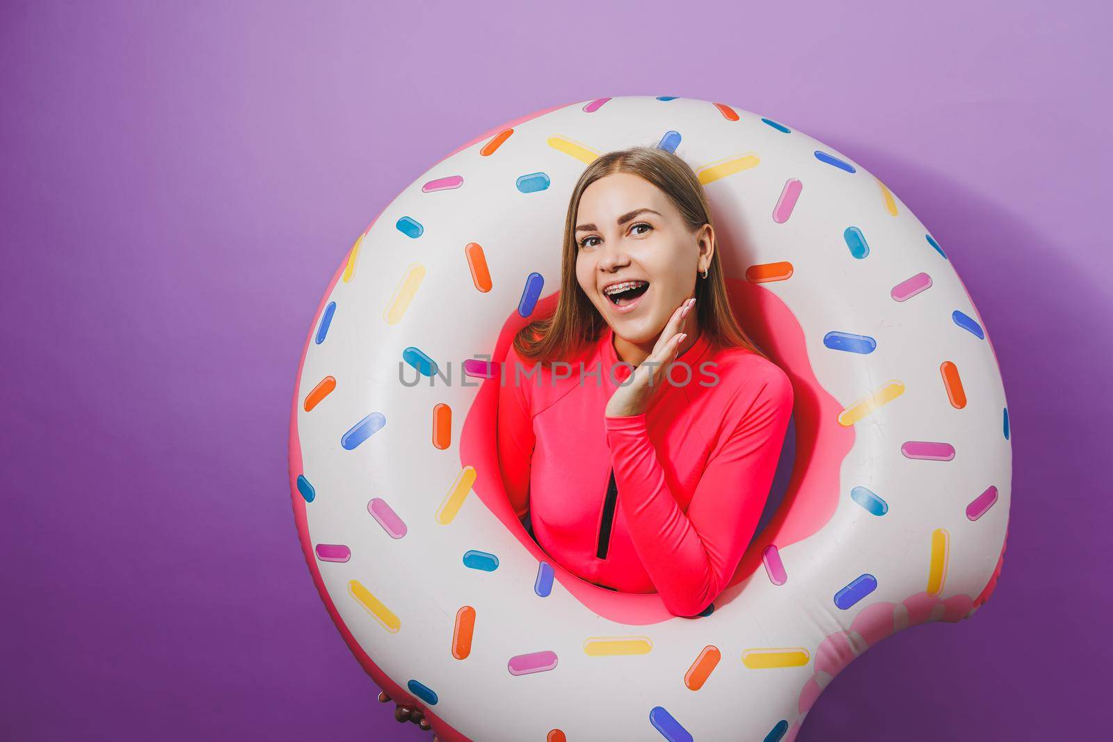 Slim young woman in a stylish pink swimsuit with a donut inflatable ring on a plain background. by Dmitrytph