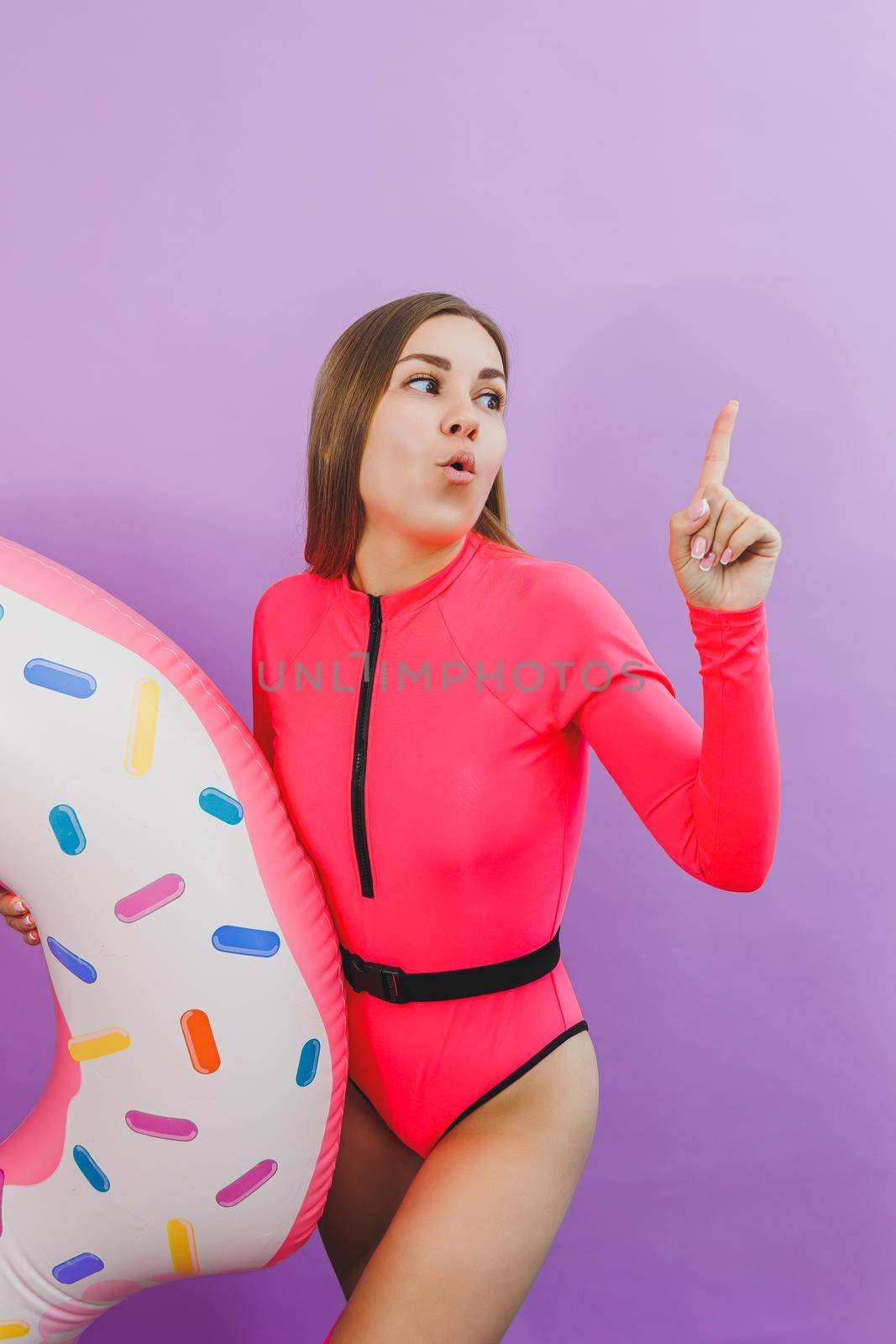 Attractive emotional woman in stylish pink swimsuit with donut inflatable ring on plain background. Beach fashion by Dmitrytph
