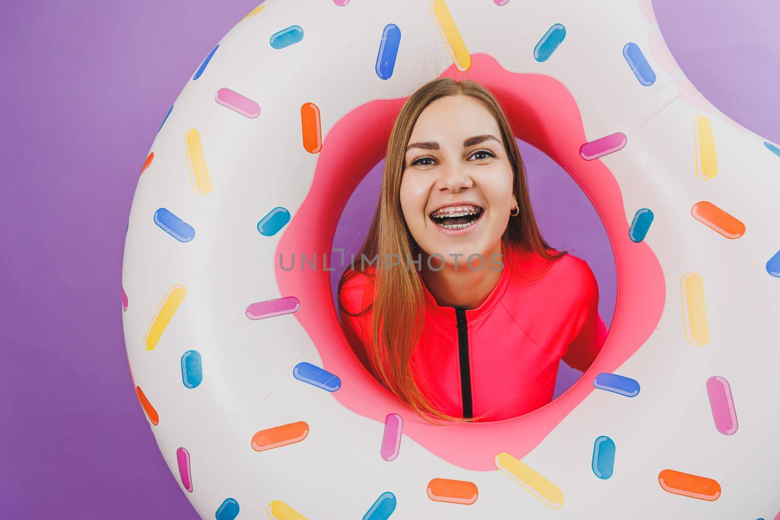 Attractive emotional woman in stylish pink swimsuit with donut inflatable ring on plain background. Beach fashion by Dmitrytph