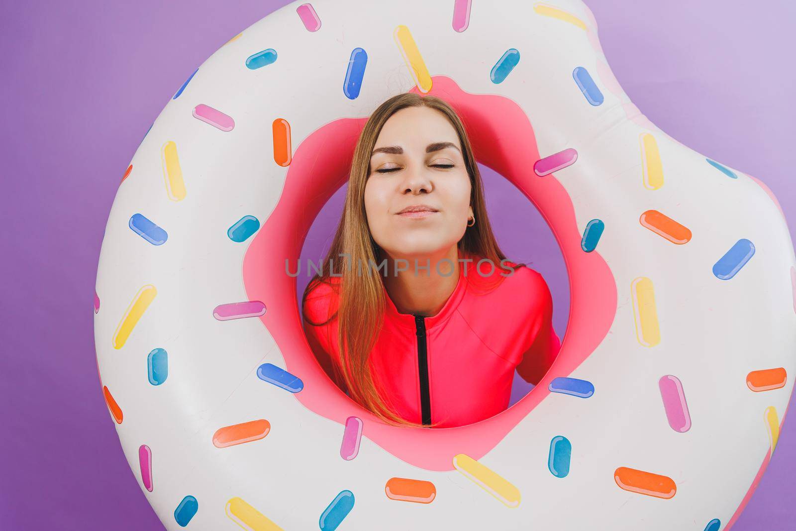 Attractive emotional woman in stylish pink swimsuit with donut inflatable ring on plain background. Beach fashion by Dmitrytph