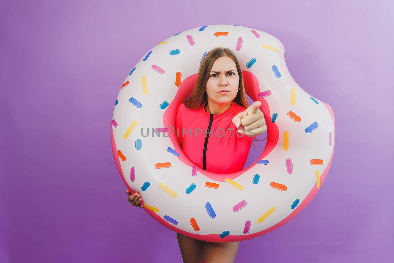 Attractive emotional woman in stylish pink swimsuit with donut inflatable ring on plain background. Beach fashion