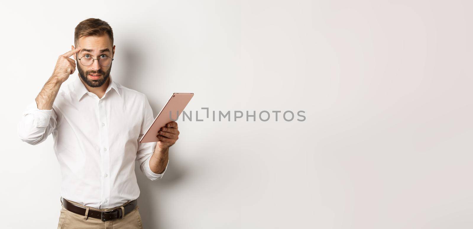 Displeased employer scolding staff while checking report on digital tablet, pointing at head and looking disappointed, standing over white background by Benzoix