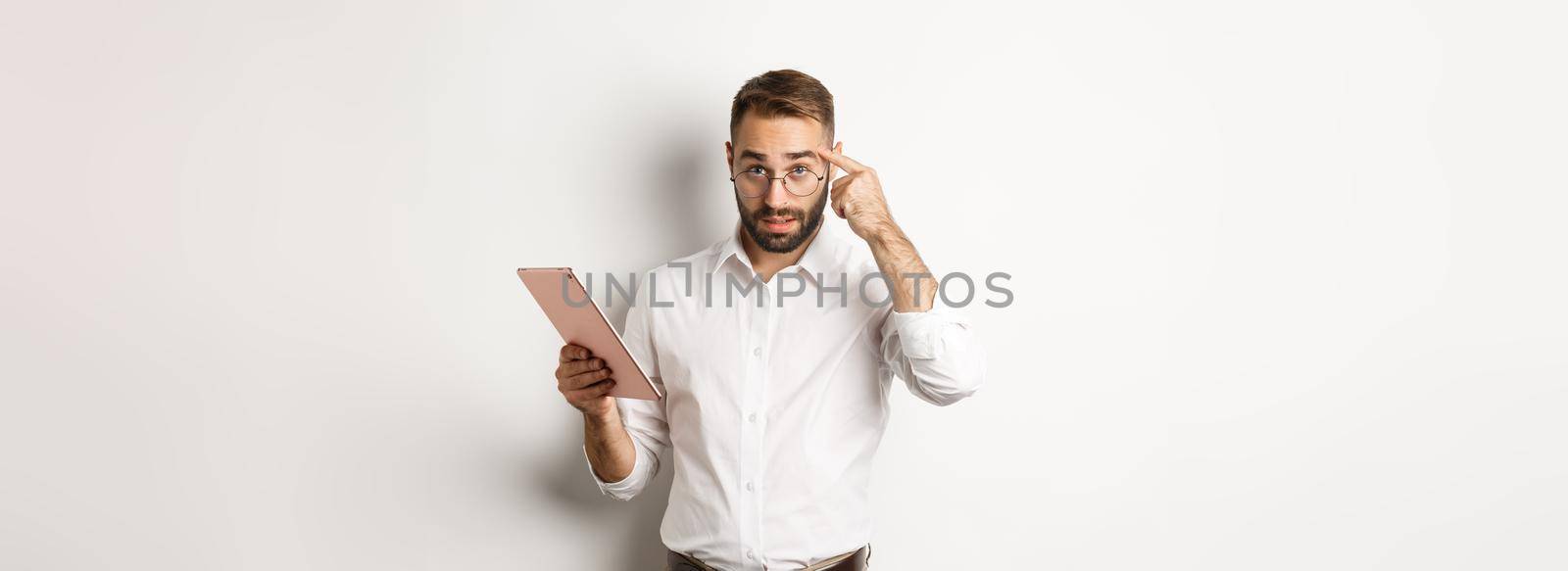 Displeased employer scolding staff while checking report on digital tablet, pointing at head and looking disappointed, standing over white background.