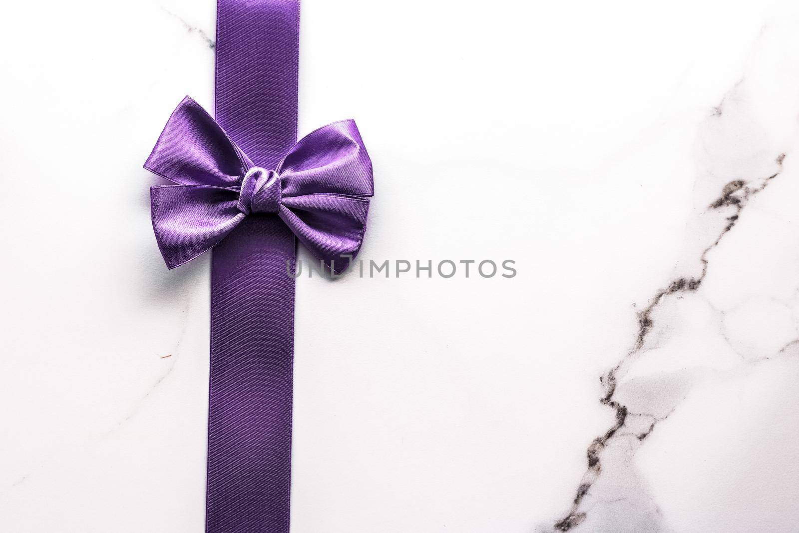 Happy holidays, festive decoration and brand sale promotion concept - Purple silk ribbon and bow on luxury marble background, holiday flatlay backdrop