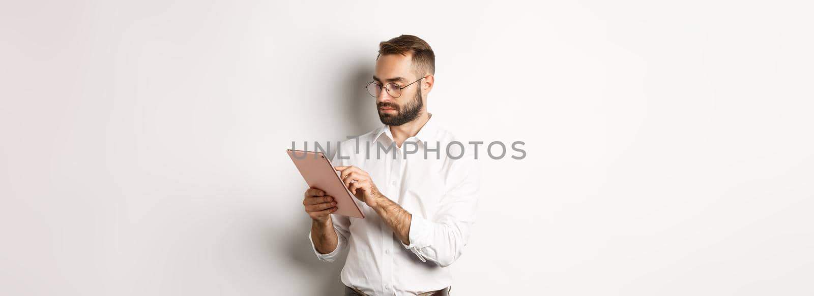 Businessman working on digital tablet, looking busy, standing over white background.
