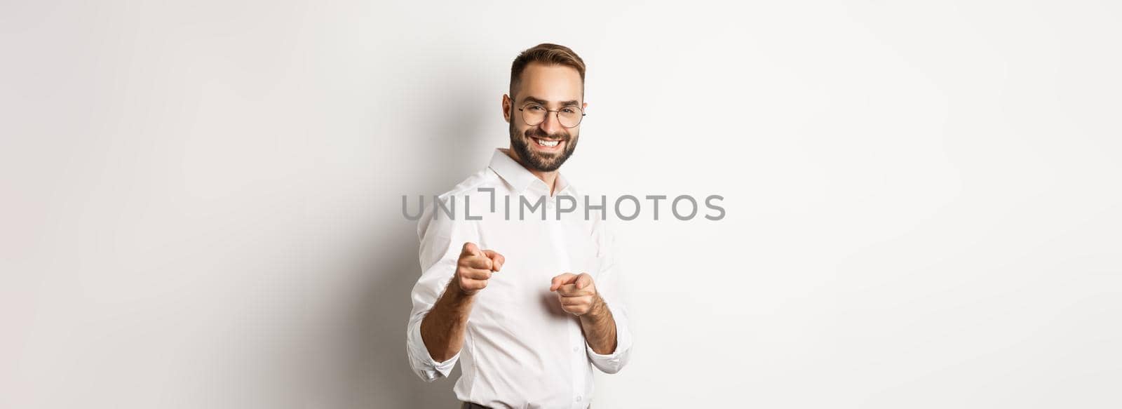 Confident businessman smiling, pointing fingers at you, congrats or praise gesture, standing over white background.