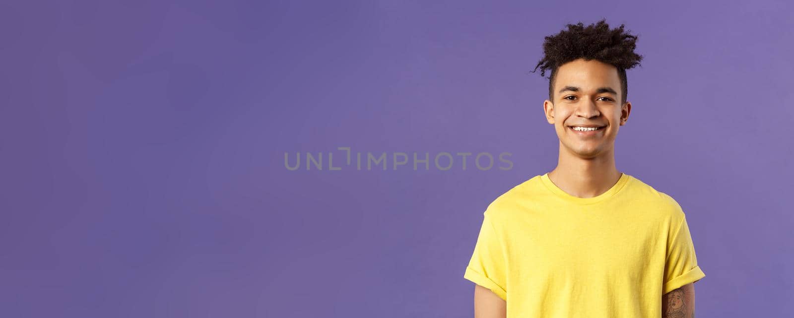Close-up portrait of nice, friendly-looking hispanic male student in yellow t-shirt, grinning delighted, look upbeat happy and positive, standing enthusiastic with beaming smile purple background.