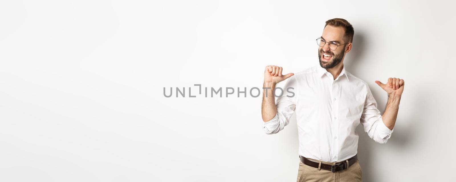 Satisfied and self-assured businessman pointing at himself, standing over white background.