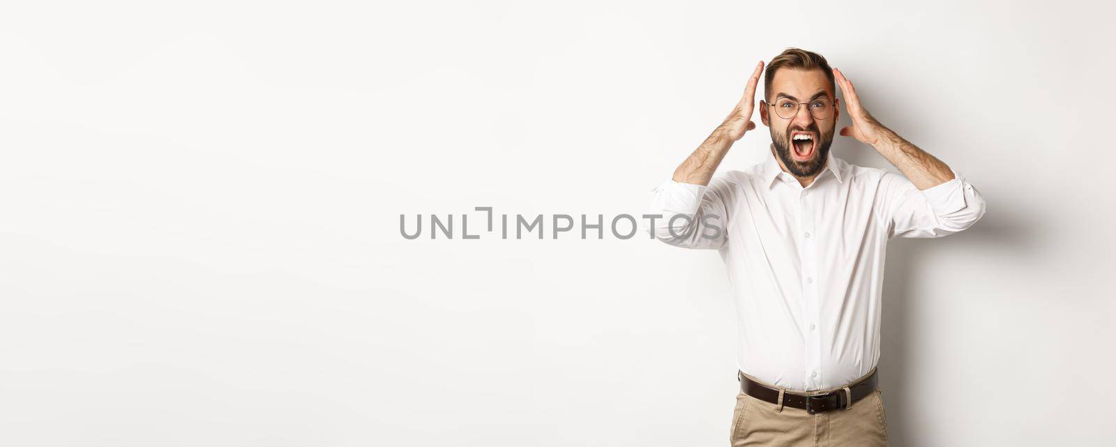 Frustrated man panicking, shouting and looking anxious, standing over white background.
