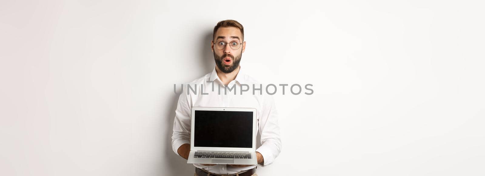 Excited businessman showing something on laptop screen, standing happy over white background.