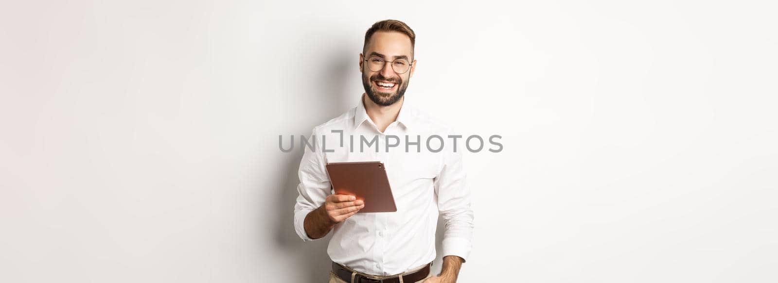 Confident business man holding digital tablet and smiling, standing against white background.