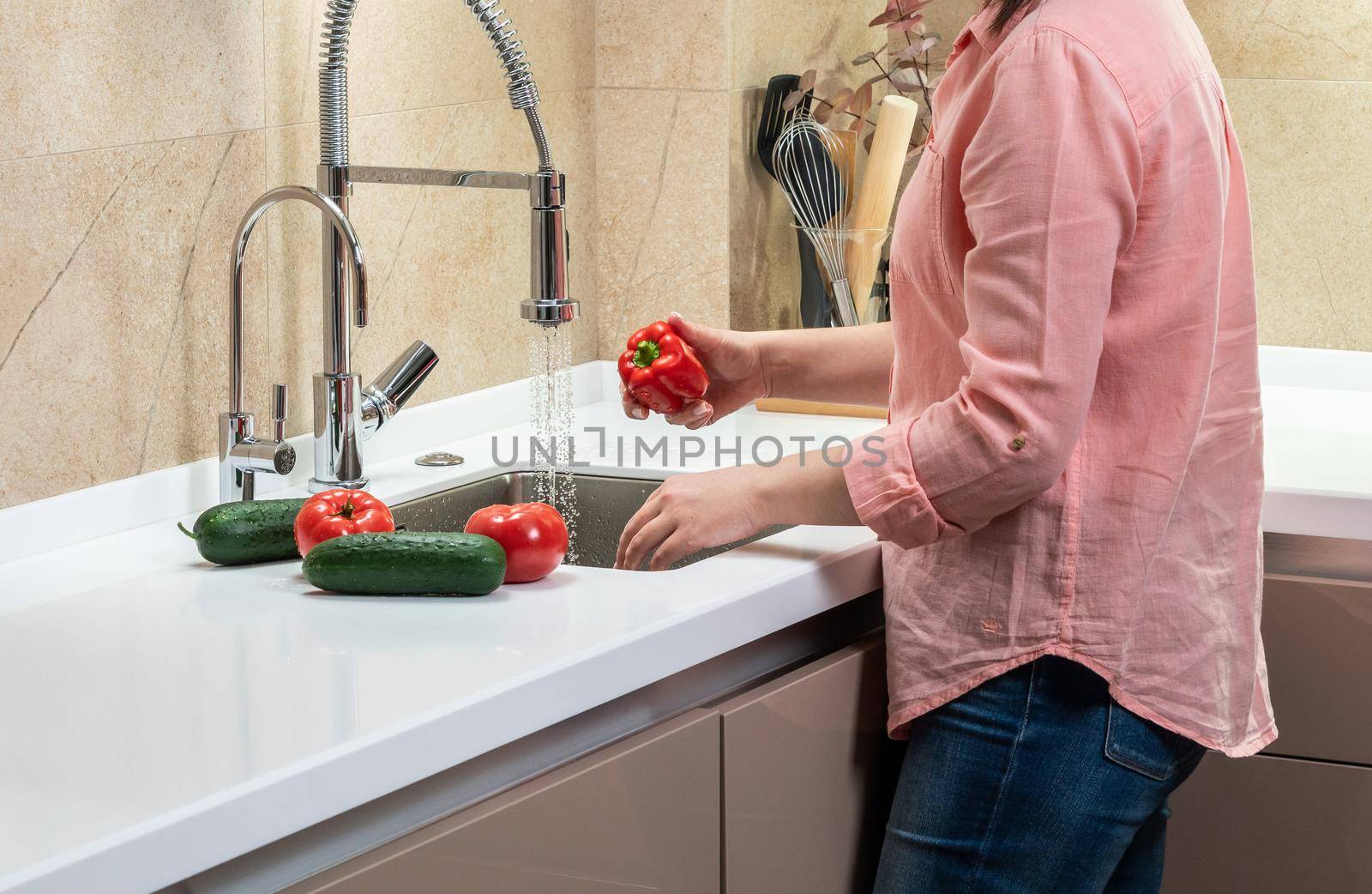 The girl washes vegetables in a beautiful bright kitchen.