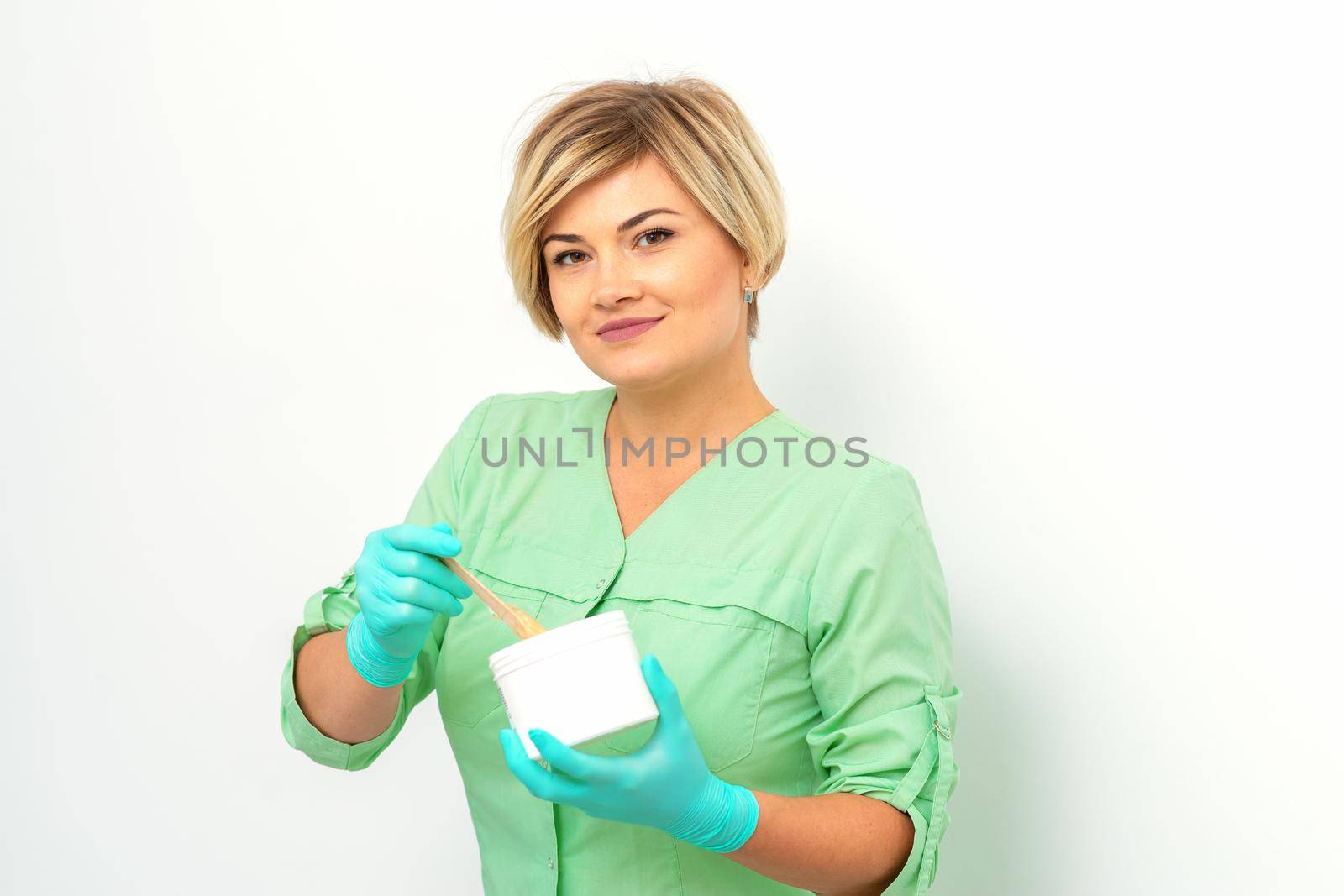 Cosmetician holding a jar of wax for depilation smiling on a white background. Natural product for hair removal. Copy space