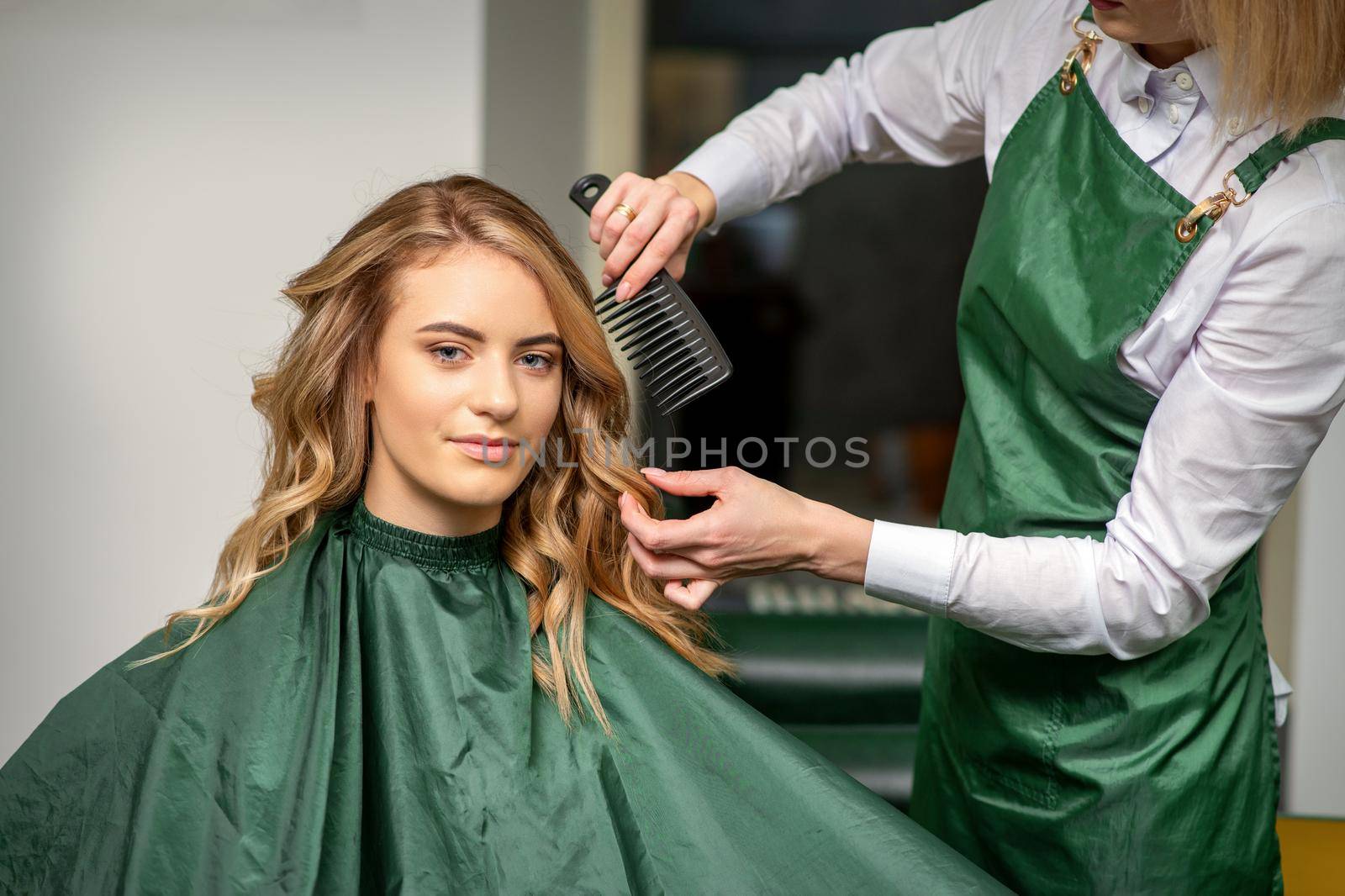 Hairdresser making hairstyling for the woman while combing with hairbrush, comb in a hair salon. by okskukuruza