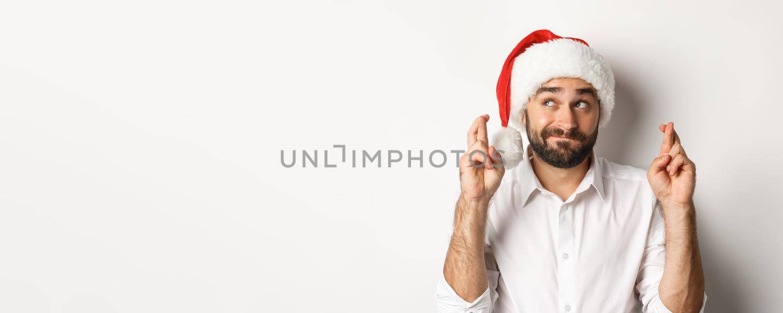 Party, winter holidays and celebration concept. Happy man in santa hat making christmas wish, cross fingers for good luck and looking hopeful at upper left corner.