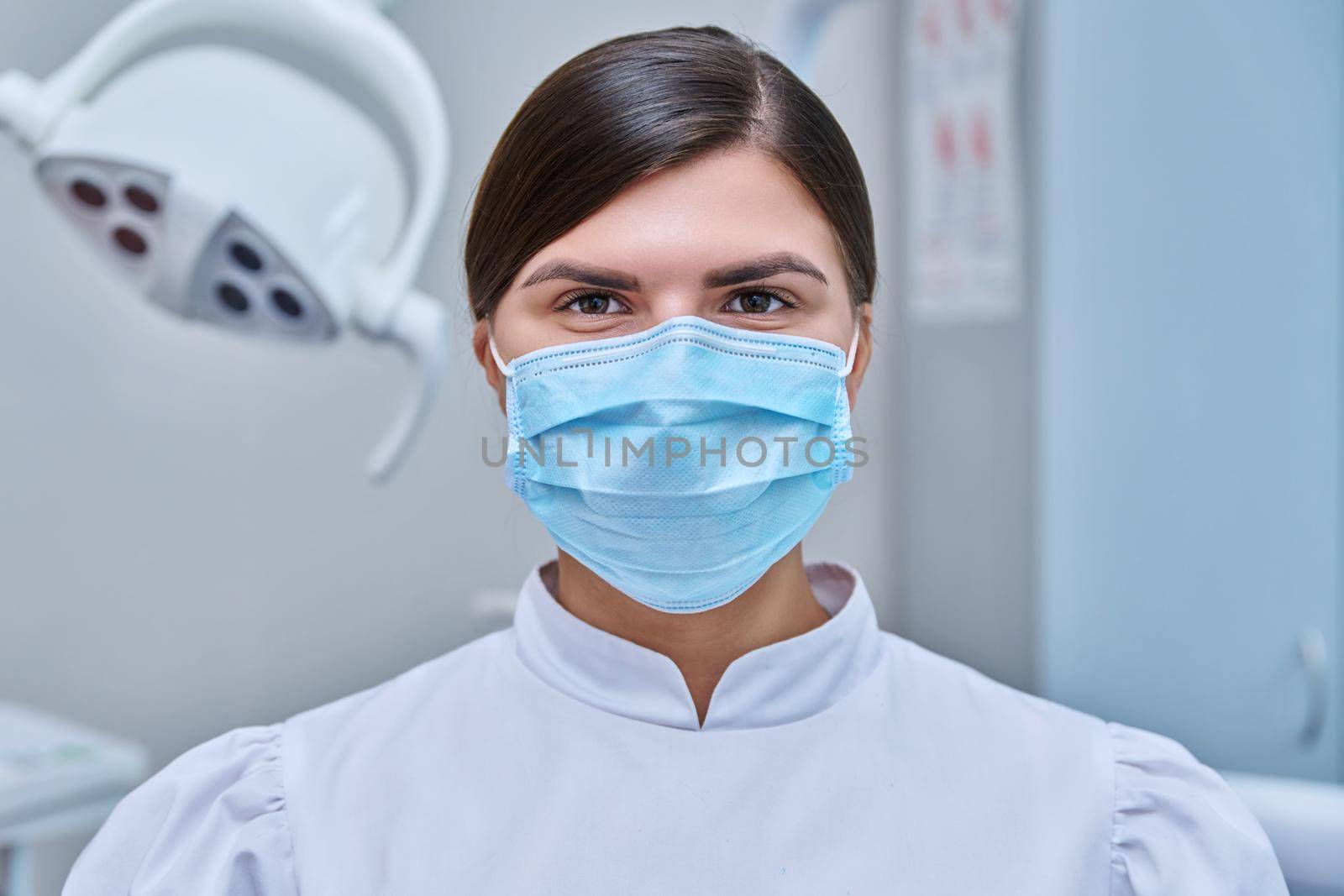 Portrait of female doctor nurse dentist in medical face mask in white by VH-studio