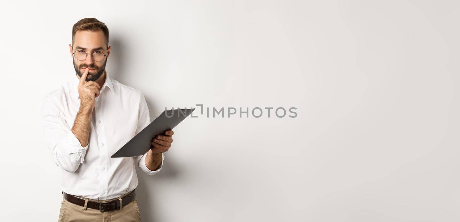 Thoughtful office employee working, holding documents on clipboard and thinking, standing over white background.