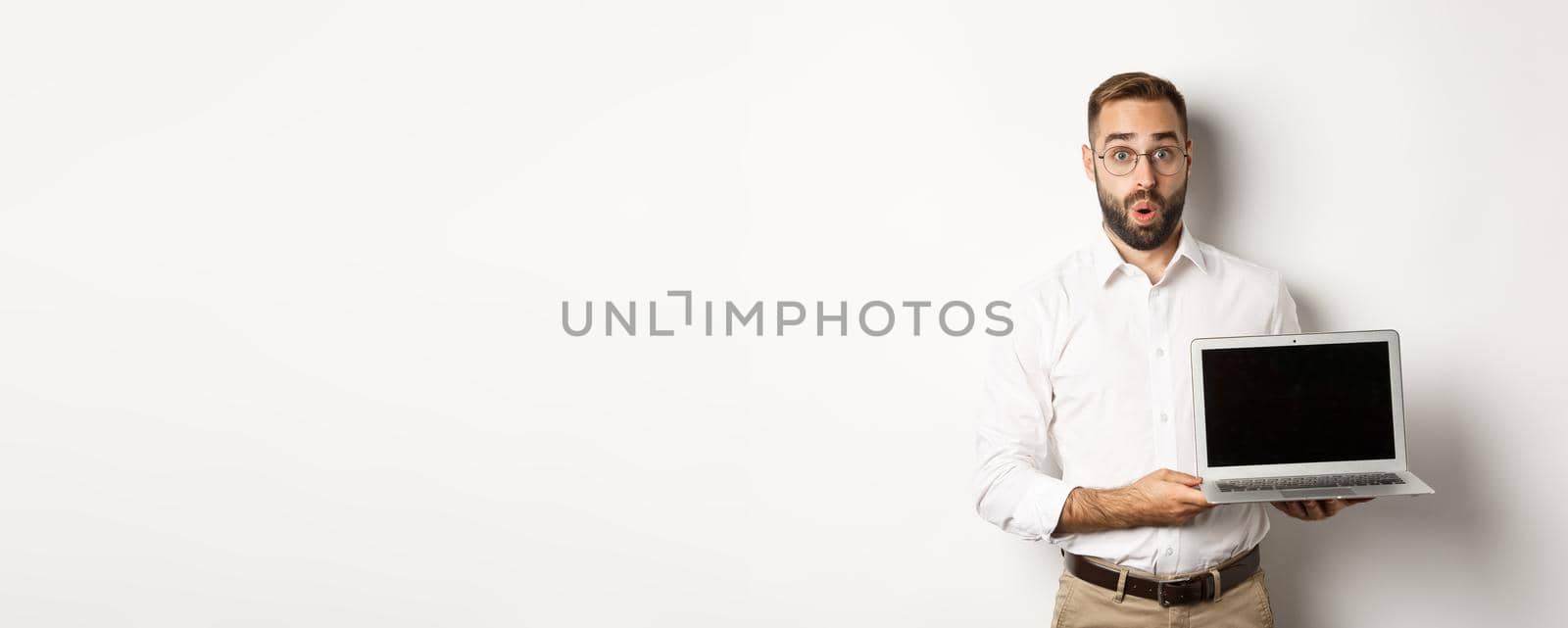 Amazed businessman showing laptop screen, standing against white background.