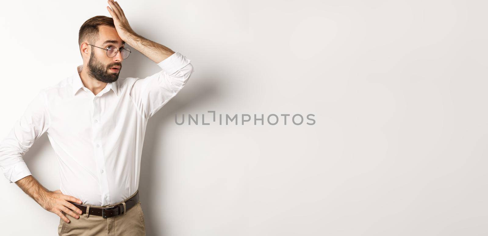 Annoyed man manager roll his eyes and slap forehead, facepalm from something tiresome, standing over white background.