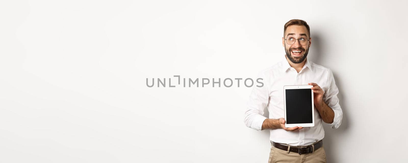 Shopping and technology. Thoughtful man showing digital tablet screen, looking at upper left corner and thinking, standing over white background by Benzoix