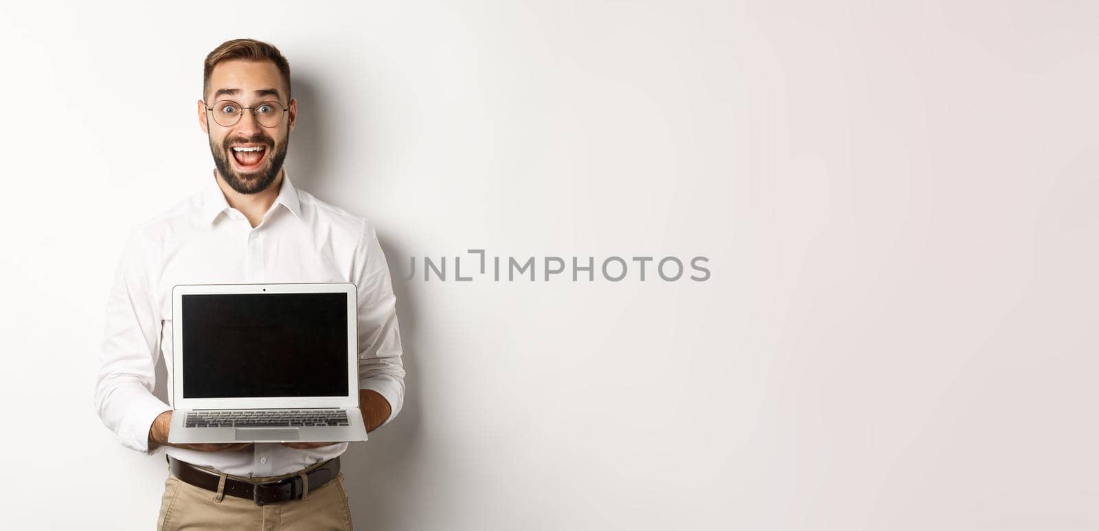 Excited businessman showing something on laptop screen, standing happy over white background.