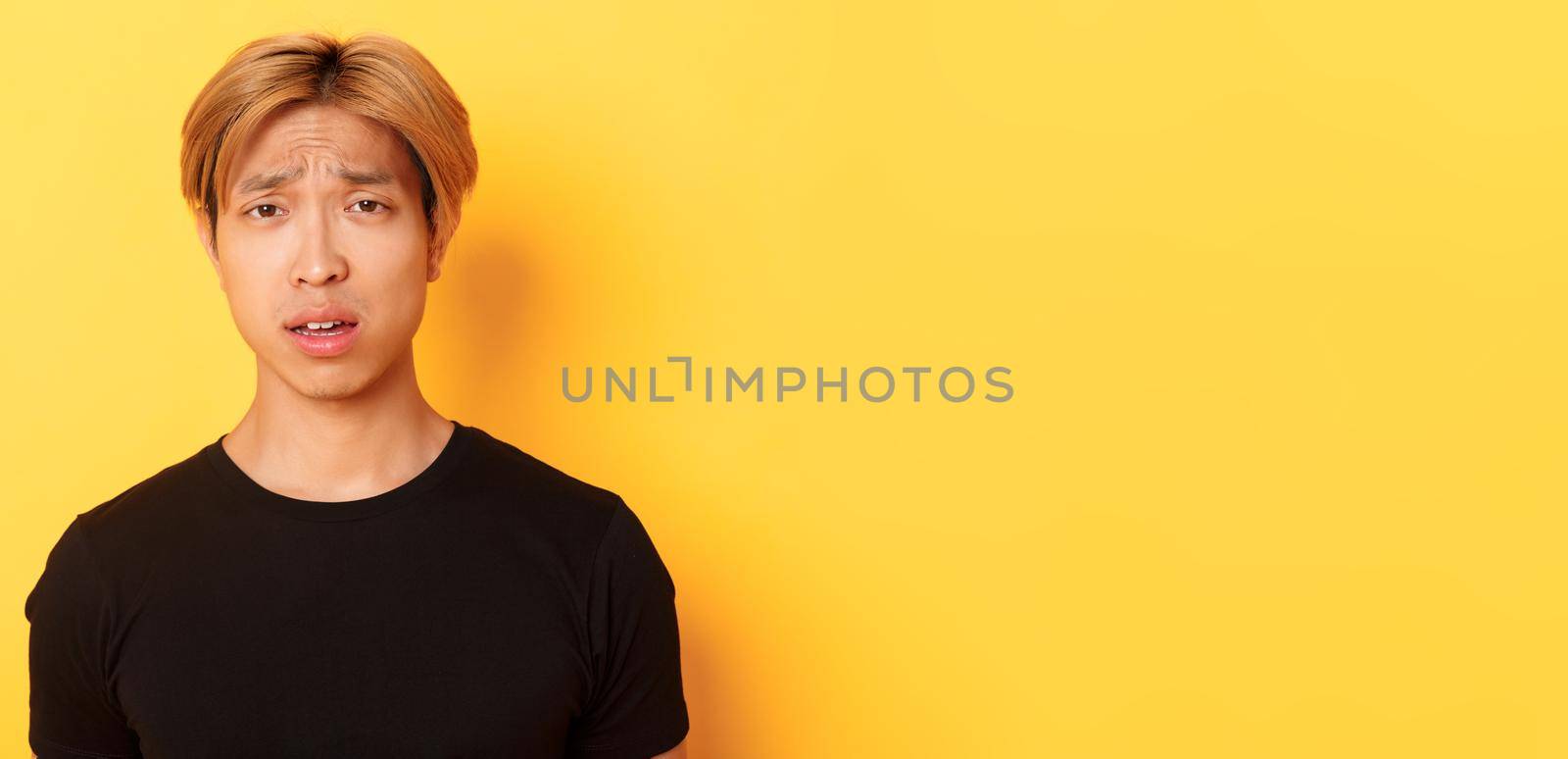 Close-up of confused and upset asian blond guy looking puzzled, open mouth and frowning perplexed, standing over yellow background by Benzoix