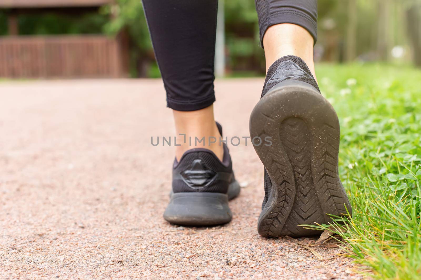 Close-up of a womans legs, in black sneakers and black leggings, walking along a path made of small red stone