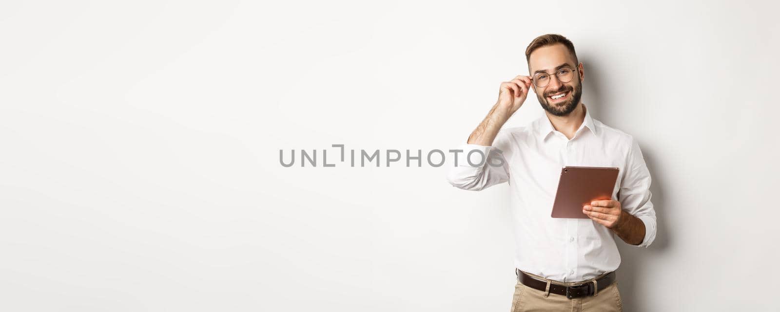 Confident business man working on digital tablet, smiling happy, standing over white background.