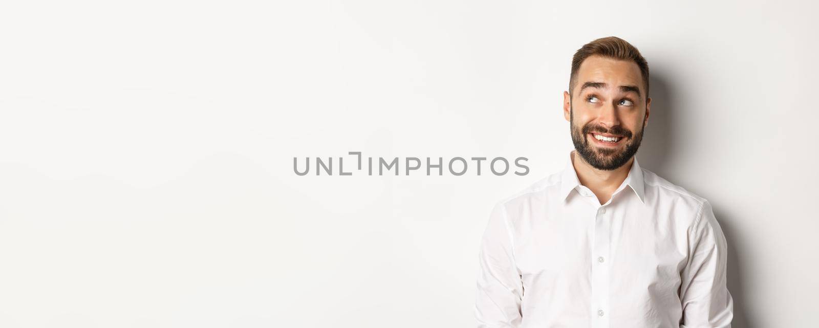 Close-up of handsome man with beard, looking thoughtful at upper left corner, imaging and smiling, white background.