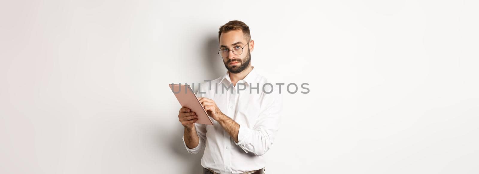 Handsome businessman doing job on digital tablet, reading something, standing over white background.