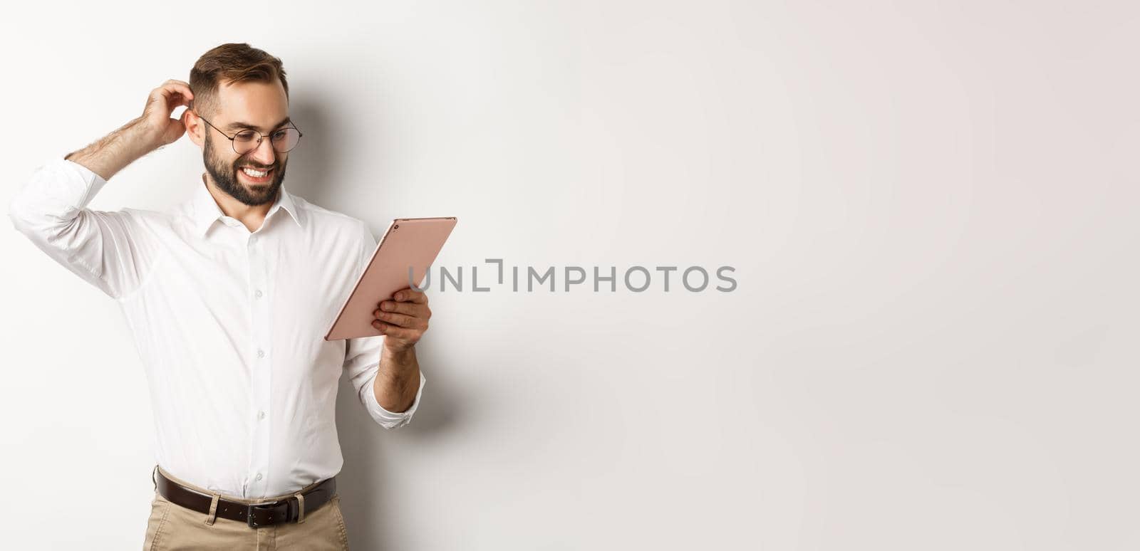 Confused male manager looking puzzled at digital tablet, scratching head doubtful, standing over white background by Benzoix