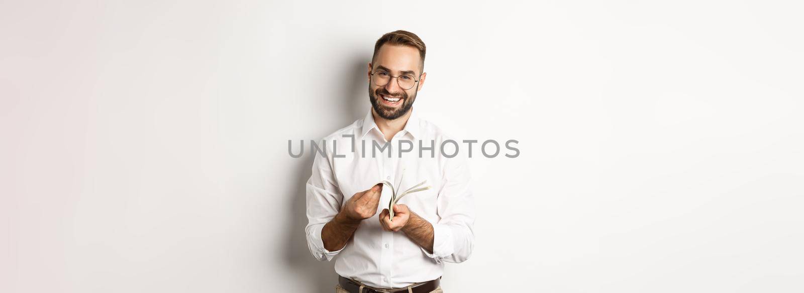 Successful businessman in white shirt, counting money and smiling satisfied, standing over white background.