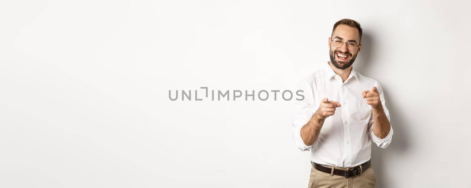 Satisfied businessman pointing fingers at camera, praising you, approve or like something, white background.